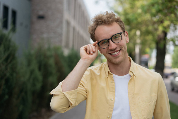 Portrait of young confident businessman wearing yellow shirt, stylish eyeglasses standing on the street. Successful smiling university student looking at camera, education concept - Fotoğraf, Görsel
