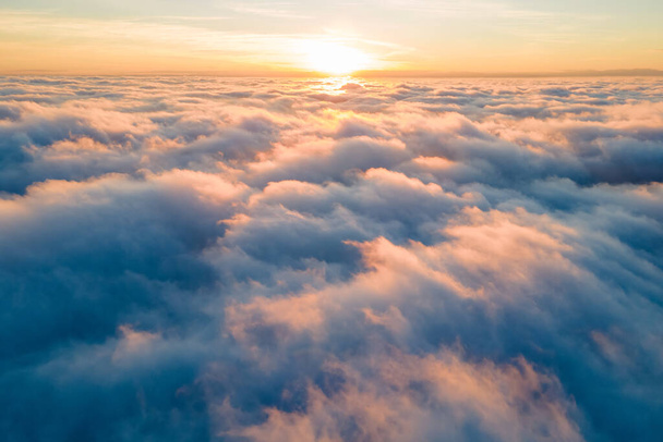 Vista aérea de la puesta de sol de color amarillo brillante sobre densas nubes blancas con cielo azul sobre la cabeza. - Foto, imagen