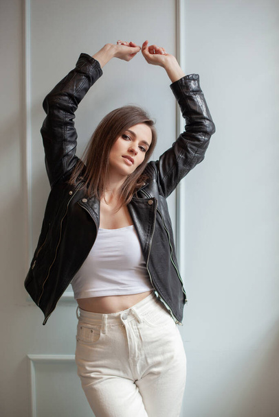 Charming young woman posing in black leather jacket and white jeans on a white background. Beauty, fashion. - Φωτογραφία, εικόνα