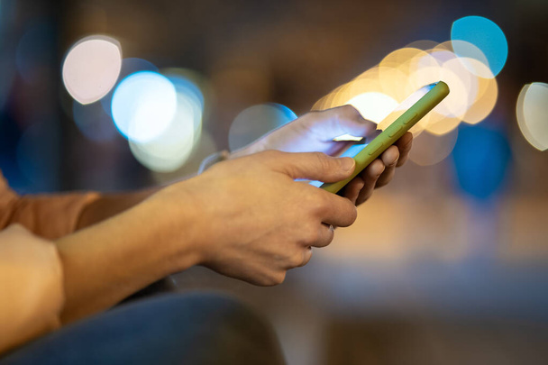 zbliżenie kobiet ręce trzymając telefon komórkowy przeglądanie Internetu na ulicy miasta z rozmytymi światłami w nocy. - Zdjęcie, obraz