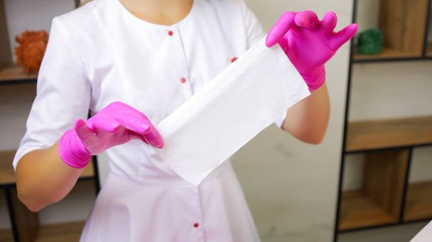 ein Mädchen, ein Meister der Zuckerepilation, steht in einem weißen Gewand und rosa Handschuhen vor einer Kundin und hält ihr eine Serviette vor - Foto, Bild