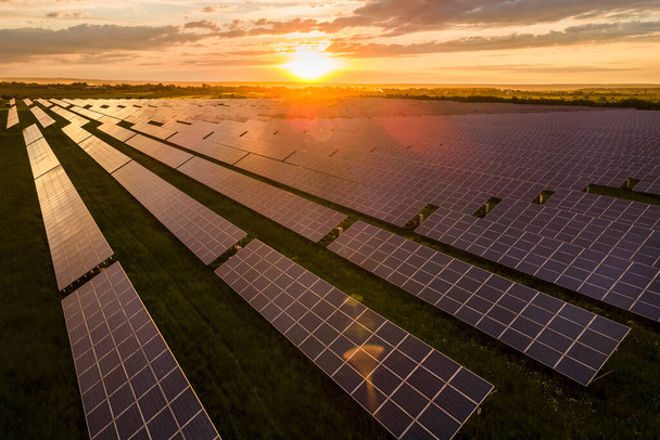 Gündoğumunda temiz ekolojik elektrik enerjisi üretmek için birçok sıra güneş fotovoltaik paneline sahip sürdürülebilir büyük elektrik santralinin havadan görüşü. Sıfır emisyon kavramı ile yenilenebilir elektrik. - Fotoğraf, Görsel