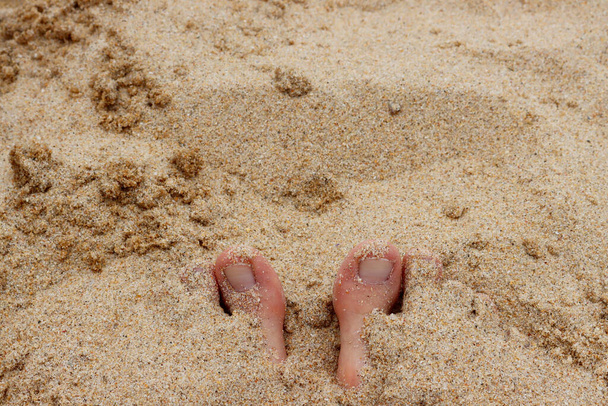 足は砂に完全に浸かり、 2本のつま先が見えます。大きなつま先はビーチの砂から突き出ています。  .  - 写真・画像