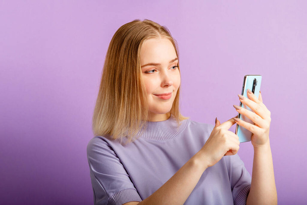 Young woman use smartphone sending message via app holding phone over isolated color purple background. - Фото, зображення