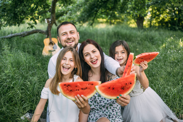 Young parents with two kids eating watermelon at picnic - Fotó, kép