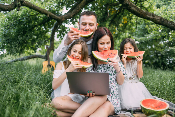 Positive family with modern laptop enjoying picnic time - Foto, afbeelding