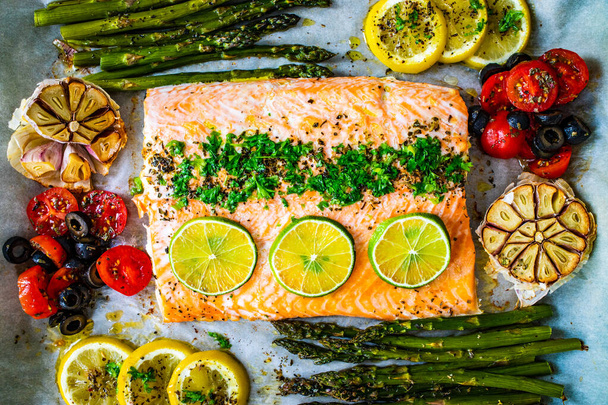 Sheet pan dinner - roasted salmon steak with asparagus, lemon ,rosemary, tomatoes, onion and garlic on cooking pan on wooden table  - Photo, image