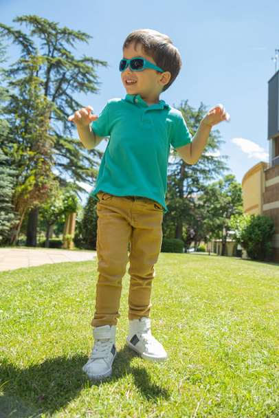 bambino sorridente con le braccia alzate mentre salta sull'erba in un giardino in una giornata di sole - Foto, immagini