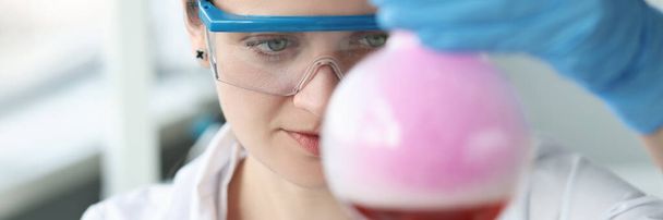 Donna ricercatrice in occhiali sta conducendo esperimento chimico in fiaschetta - Foto, immagini