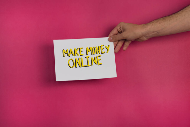 eine Nahaufnahme eines Mannes, der ein Papier mit der Aufschrift "Make Money Online" auf einem fuchsiafarbenen Hintergrund hält - Foto, Bild