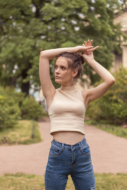 Young slender woman 18 years old stands in park with raised arms. - Foto, Bild