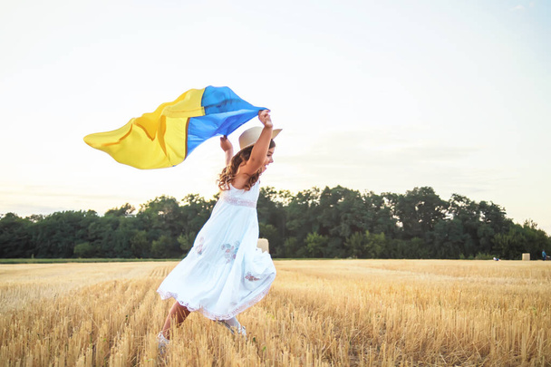 Keltainen sininen Ukrainan lippu käsissä tyttö käynnissä mangled alalla vehnää. Onnellinen lapsi Ukrainan lipun kanssa. Itsenäisyyspäivä. Lippupäivä. Perustuslakipäivä - Valokuva, kuva