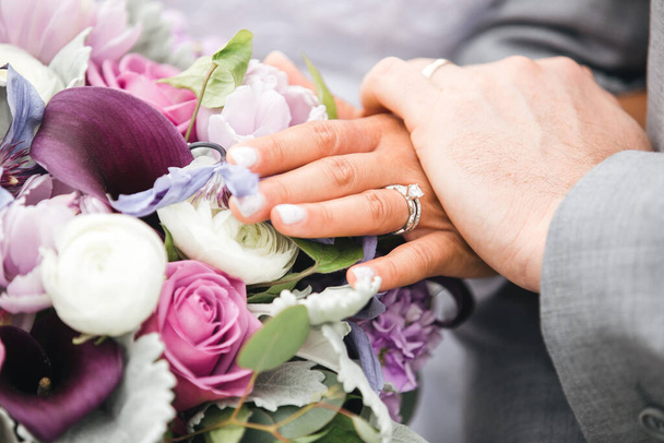 Close up de mãos de noiva e noivo com anéis de casamento em buquê de noiva com rosas, peônias e lírios. - Foto, Imagem