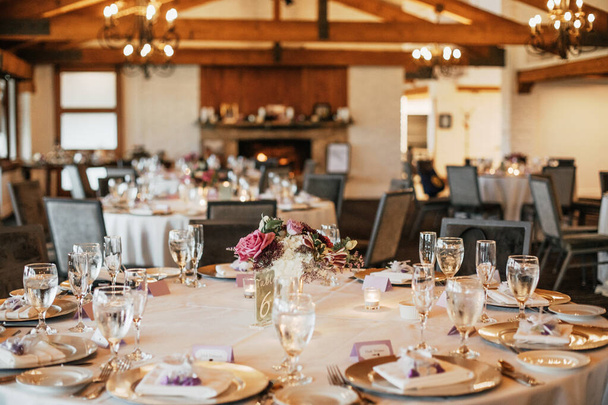 白いテーブルクロス、ガラス製品、フラワーアレンジメントセンターピースと暖炉のある美しい結婚式会場. - 写真・画像