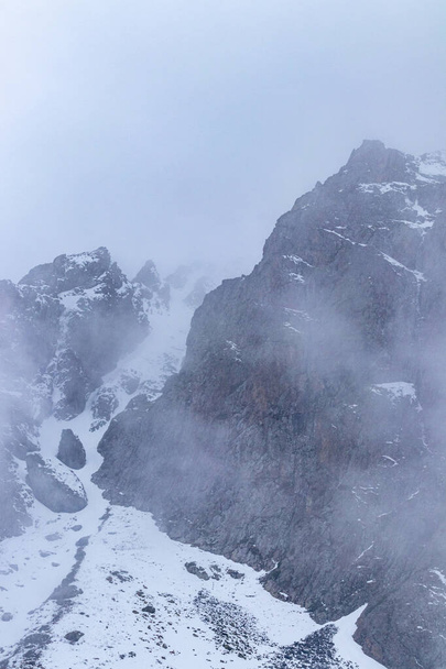 El acantilado de la montaña está en la niebla, y hay nieve al pie. Invierno - Foto, imagen