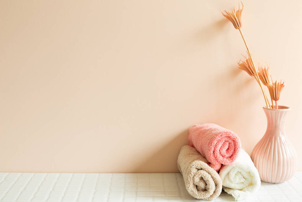 Полотенце в ванной, ваза растения на белом мозаичном столе. розовый фон стены. Концепция ухода за кожей и спа. Интерьер дома - Фото, изображение