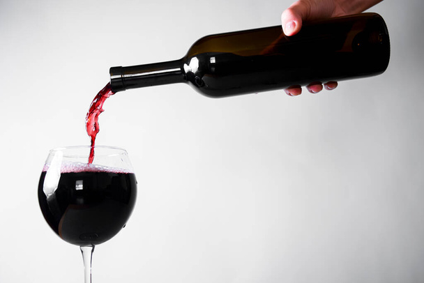 Red wine pouring down from a wine bottle into a wine glass over white background. Banner with copy space. Wine concept. - Φωτογραφία, εικόνα