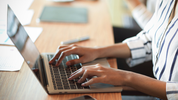 Vista lateral da mulher de negócios inteligente digitando, trabalhando, navegando no teclado do laptop na mesa de madeira com interior de escritório embaçado no fundo  - Foto, Imagem