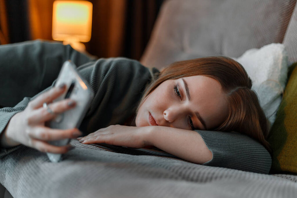 不眠症のサーフィンインターネットに苦しむか、ベッドの上に横に夜にスマートフォンを使用してチャット悲しい十代の少女。うつ病インターネット中毒。若い女性のうつ病 - 写真・画像