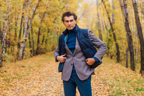 Tall handsome man dressed in a brown jacket walking in the autumn alley - Foto, imagen