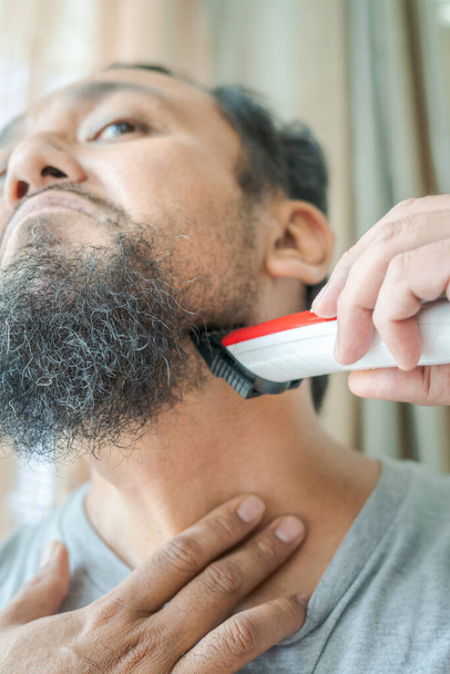 Asian man shaving beard with electric razor machine. - Photo, Image