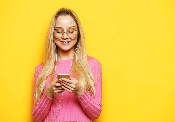 Photo of cheerful cute beautiful young woman wearing pink sweater and glasses chatting by mobile phone - Photo, Image