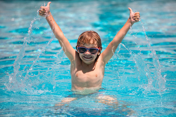 Child boy with thumbs up raised hands swim in swimming pool. splashing in water having fun leisure activity open arms. - Zdjęcie, obraz