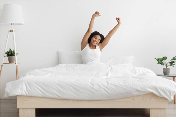 Хорошее начало нового дня. Проснувшаяся африканская американка простирает руки после пробуждения, чувствуя себя счастливой - Фото, изображение