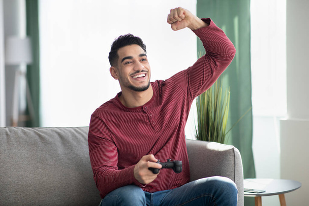 Щасливий арабський чоловік сидить на дивані у вітальні, ігровий
 - Фото, зображення