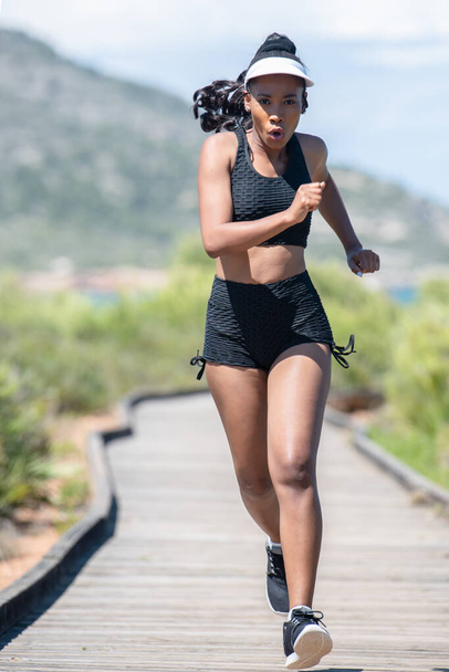 Femme afro-américaine vigoureuse s'exerçant le long d'une piste en bois : foyer sélectif. concept mode de vie. - Photo, image