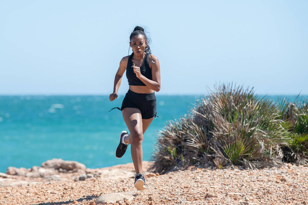 Афро-американка энергично бегает у моря: упражнения и концепция силы. Селективный фокус. - Фото, изображение