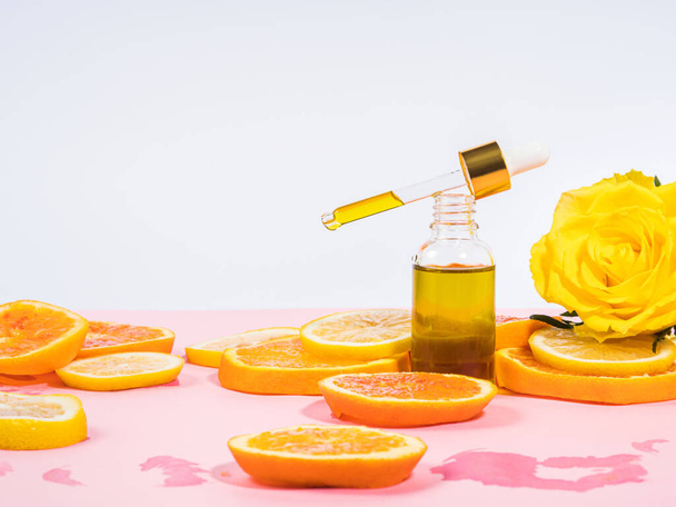 Frasco de soro de vitamina C com conta-gotas em fundo rosa com fatias de citrinos laranja - Foto, Imagem