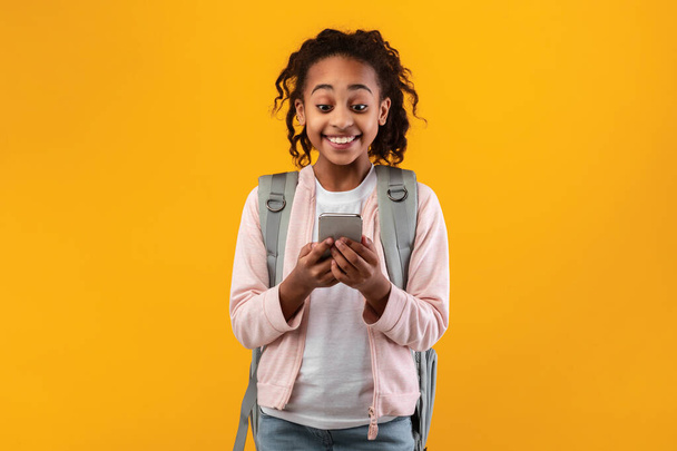 Συναρπαστικό μαύρο κορίτσι που χρησιμοποιεί το κινητό τηλέφωνο στο κίτρινο στούντιο - Φωτογραφία, εικόνα