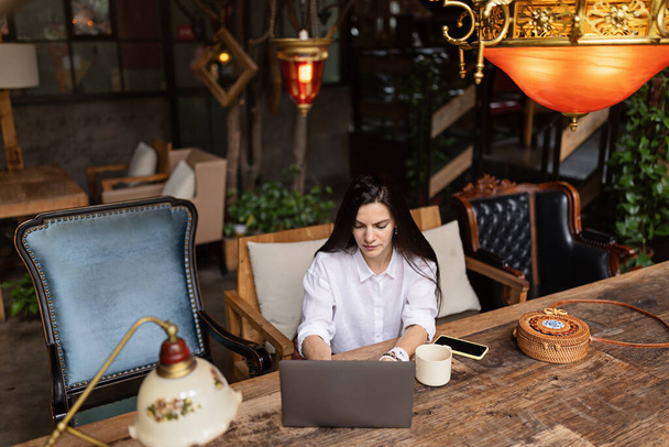 Young Caucasian business woman with long brunette hair working on laptop in cafe. College student using technology , online education, freelance  - Foto, Bild