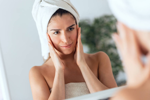 Portrait of beautiful young woman caring of her skin while putting on cream looking at mirror at home. - Foto, Bild