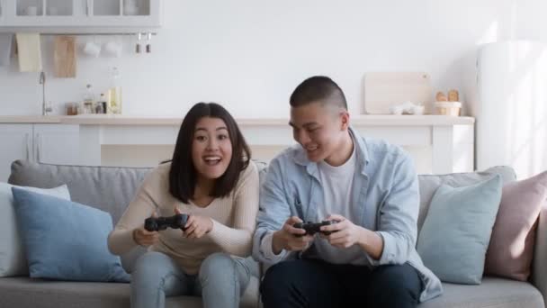 Счастливая китайская пара играет в видеоигру, развлекаясь дома - Кадры, видео