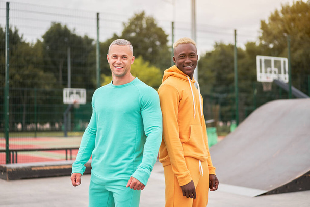 Multi-ethnic friendship Black african-american and caucasian guy friends spending time together on skate park Two multi ethnic student Dressed colorful sportswear. - Foto, immagini