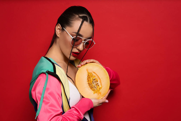 Young woman with fresh melon on red background, space for text. Exotic fruit - Foto, imagen