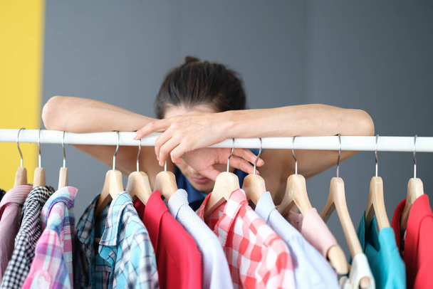 Pensive woman stands near hanger with clothes - Foto, imagen
