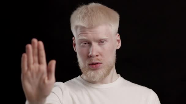 Albino guy gesturing stop a camera posa su sfondo nero - Filmati, video