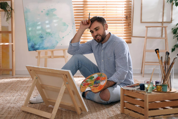 Young man painting on easel with brush in artist studio - Фото, зображення