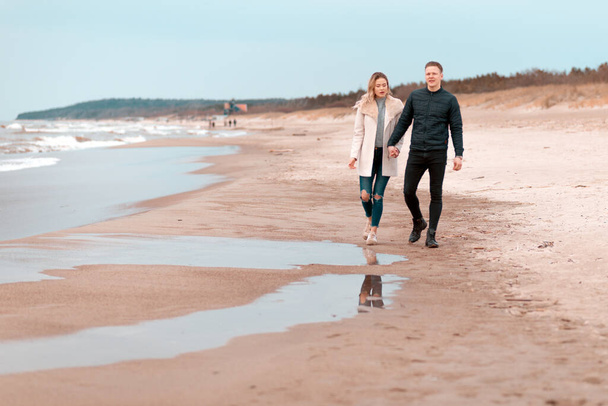 Houkutteleva nuori pari kävelee hiekkarannan rannalla, kevään romanttisella lomalla, ulkona. Matkailijoiden elämäntapa. Pari nauttii rakastava aikaa yhdessä. - Valokuva, kuva