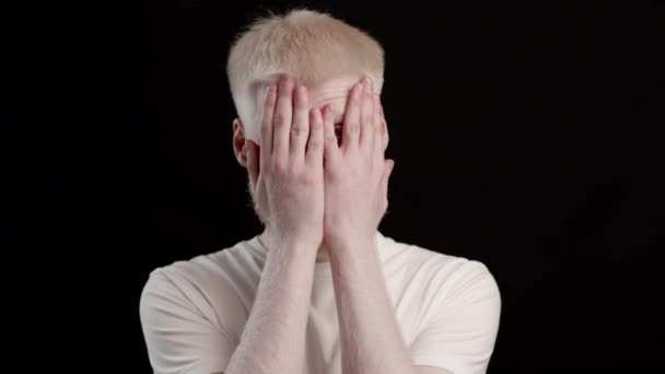 Albino άνθρωπος που καλύπτει το πρόσωπο κρυφοκοιτάζοντας μέσα από τα δάχτυλα σε μαύρο φόντο - Πλάνα, βίντεο