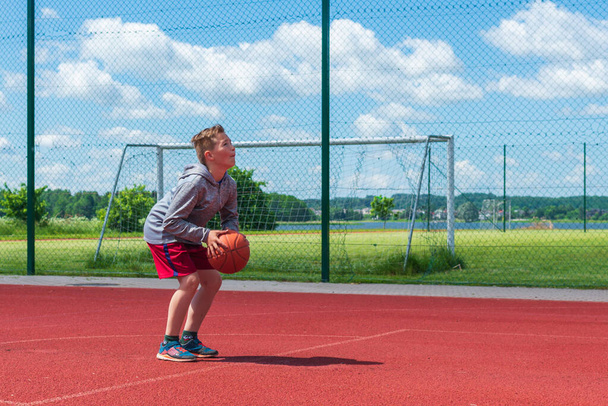 Çocuk oyun sahasında basketbol atışına hazırlanıyor. Çocuk güneşli yaz günlerinde oyun sahasında basket oynuyor.. - Fotoğraf, Görsel