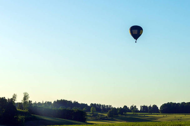Jedna silueta horkovzdušný balón v modré obloze krajiny pozadí.Horkovzdušný balón nad zeleným polem. - Fotografie, Obrázek