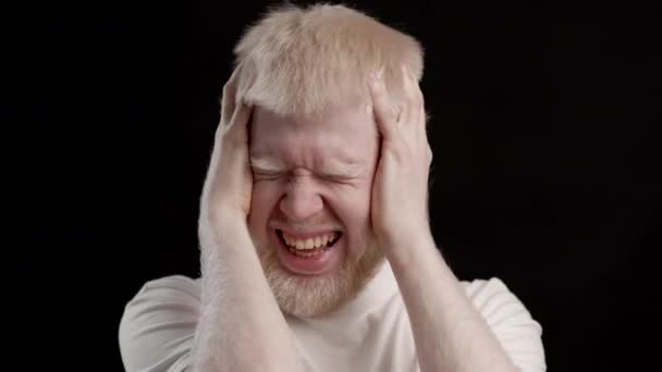 Albino chico sacudiendo cabeza cubriendo oídos teniendo dolor de cabeza, fondo negro - Imágenes, Vídeo