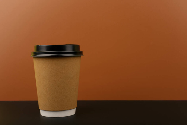 Close up of brown cardboard cup with tea or coffee on black table against brown background with copy space. Concept of hot drinks for take away - 写真・画像