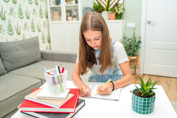 A little girl draws with felt-tip pens at home in a modern living room. Completing homework with the help of books - Foto, afbeelding