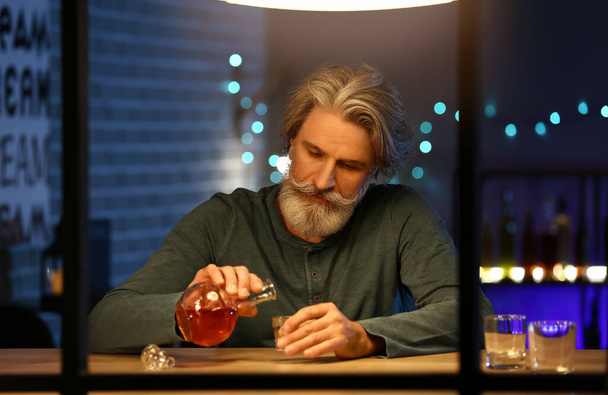 Senior man pouring drink into glass late in evening at home - Foto, afbeelding