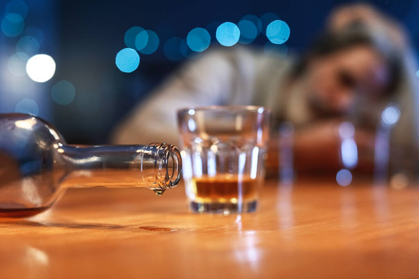 пустая бутылка виски на столе пьяного пожилого человека, крупным планом - Фото, изображение
